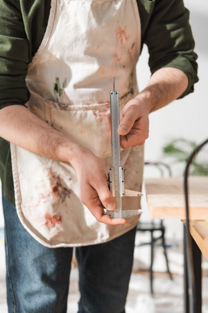 Cropped view of restorer in apron holding calipers in workshop