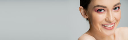 portrait of happy young woman with makeup smiling at camera isolated on grey, bannerの写真素材