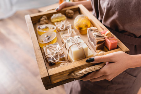 wooden tray with assortment of handmade soap in hands of cropped african american craftswomanの写真素材