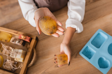 top view of cropped african american craftswoman holding handmade soap near blurred silicone mold and wooden trayの写真素材