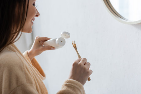 happy young woman holding tube with toothpaste and toothbrush in morningの写真素材