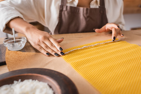 partial view of african american woman in apron holding natural twine near wax sheet on parchment in craft workshopの写真素材