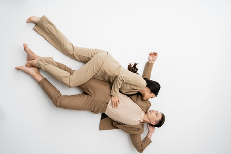 top view of barefoot multiethnic couple in fashionable pantsuits looking at each other while lying...