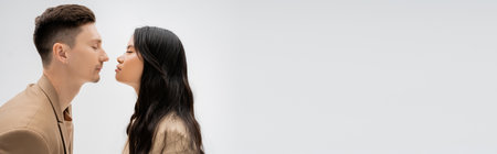 side view of long haired asian woman and trendy man posing face to face with closed eyes isolated on grey, bannerの写真素材