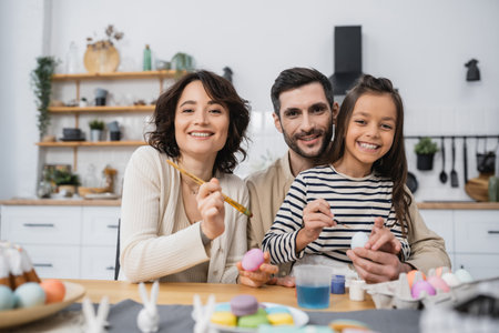 Smiling family looking at camera while coloring Easer eggs in kitchenの写真素材