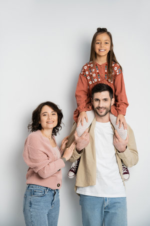 Smiling girl sitting on shoulders of father near mom on white background