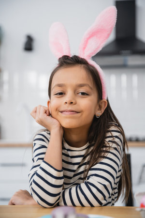 Smiling girl in Easter bunny ears headband looking at camera at home