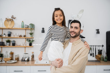 Smiling man with Easter headband holding daughter at homeの写真素材