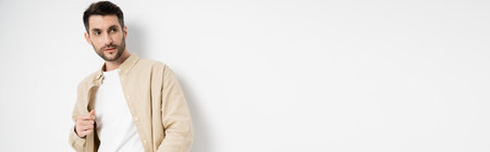 Bearded man in beige shirt looking away on white background, bannerの写真素材