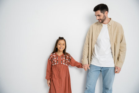 Smiling man holding hand of daughter on white backgroundの写真素材