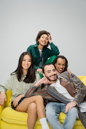 happy african american woman looking away near multiethnic friends sitting on yellow sofa isolated...