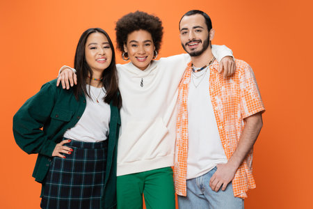 cheerful african american woman embracing trendy multiracial friends isolated on orangeの写真素材
