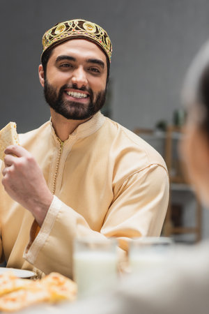 Smiling muslim father holding pita bread near blurred daughter at homeの写真素材