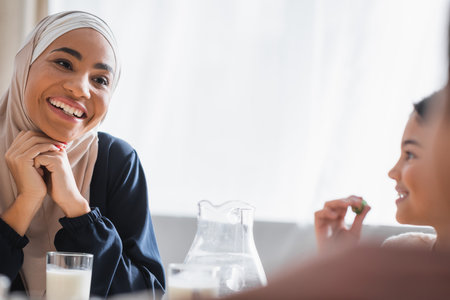 Happy african american mother in hijab looking at blurred kids during suhur at homeの写真素材