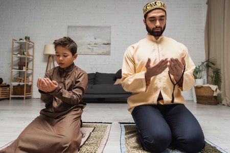 Muslim man and son praying on rugs during ramadan at homeの写真素材
