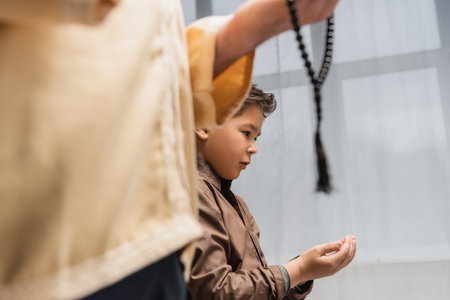 Middle eastern boy praying near blurred dad with prayer beads at homeの写真素材