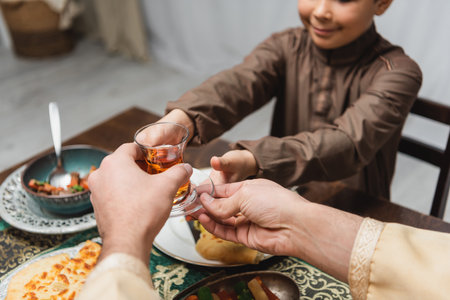 Cropped view of muslim man giving turkish tea glass to son during iftar at homeの写真素材