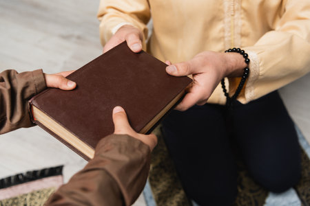 Cropped view of muslim man with prayer beads giving book to son at homeの写真素材