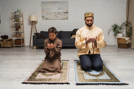 Muslim father and son praying on rugs at homeの写真素材