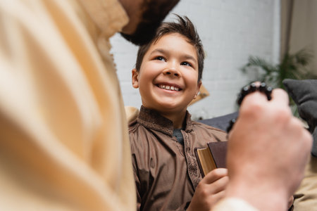 Blurred muslim dad with prayer beads near smiling son holding book at homeの写真素材