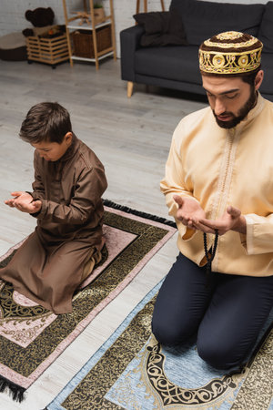 Muslim father with prayer beads praying near son at homeの写真素材