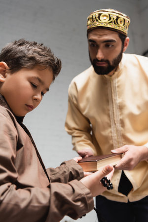Blurred muslim father giving book to son with prayer beads at homeの写真素材