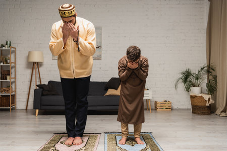 Barefoot muslim father and boy praying on rugs at homeの写真素材