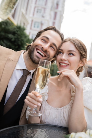 joyful and young newlyweds holding glasses of champagne during wedding celebrationの写真素材