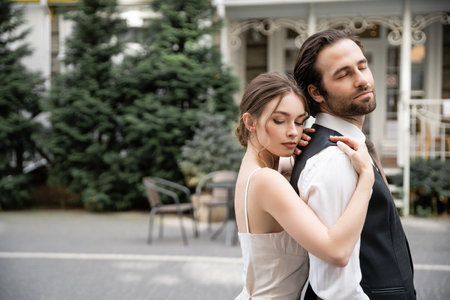young woman in wedding dress hugging bearded groom in vestの写真素材