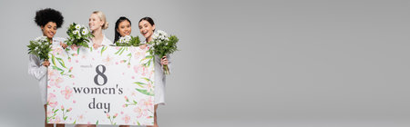 young multicultural women smiling near flowers and mothers day greeting placard isolated on grey, bannerの写真素材
