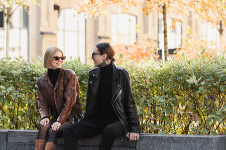 happy and stylish couple in sunglasses and leather jackets sitting outdoors during dateの写真素材