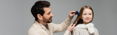 happy bearded father brushing hair of smiling daughter isolated on grey, bannerの写真素材