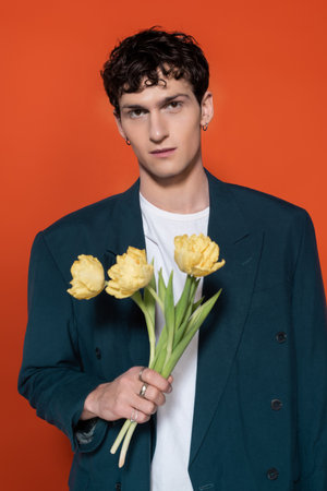 Portrait of stylish brunette man holding yellow tulips isolated on red