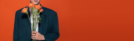 Cropped view of man in blazer holding orange roses for 8 march isolated on red, bannerの写真素材