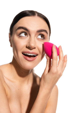 amazed young woman with natural makeup holding pink beauty sponge isolated on whiteの写真素材