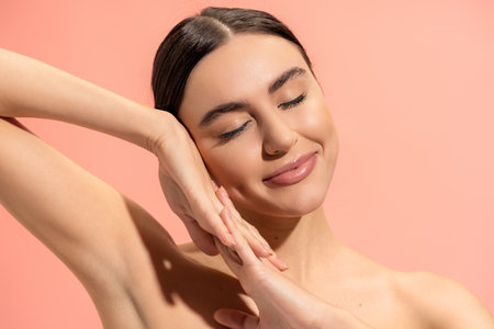 pleased woman with clenched hands and closed eyes posing isolated on pinkの写真素材