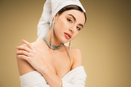 sensual woman with makeup and white towel on head touching bare shoulder on beige backgroundの写真素材