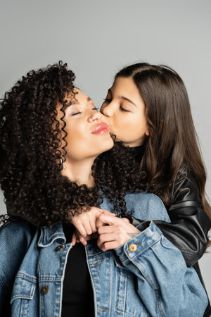 Child kissing and hugging curly mother isolated on greyの写真素材