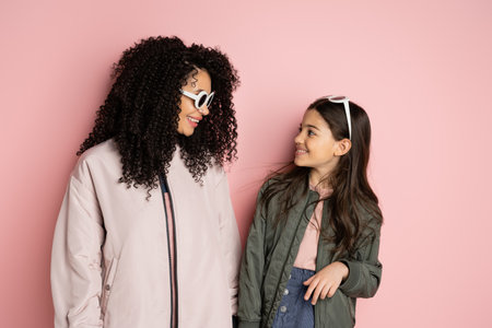 Smiling preteen girl in sunglasses looking at mom on pink background