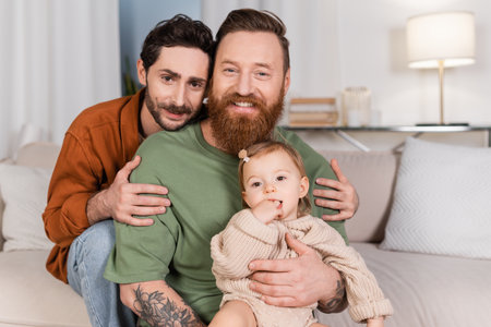 Smiling gay man hugging partner with baby daughter at home