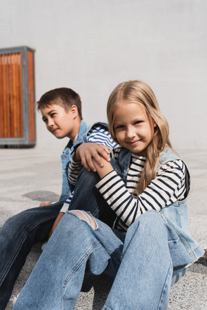 well dressed and cheerful girl in denim vest sitting near stylish boyの写真素材
