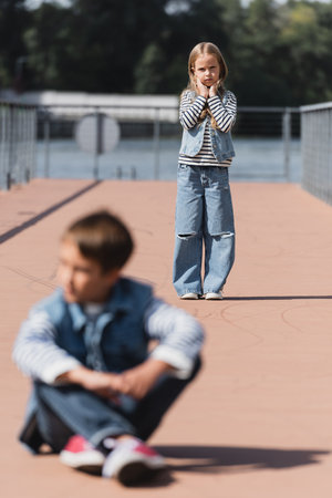 full length of preteen girl in denim outfit standing on river embankment near blurred boy on foregroundの写真素材