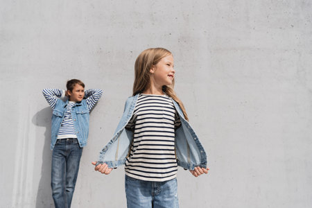 cheerful girl in denim outfit standing near well dressed boy on blurred backgroundの写真素材