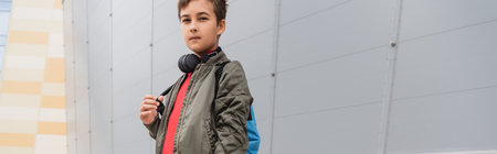 preteen boy in wireless headphones standing with backpack near mall, bannerの写真素材