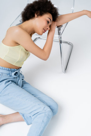 High angle view of young african american woman sitting near chair on grey backgroundの写真素材