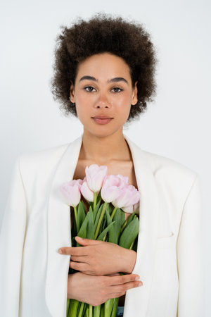 Young african american woman in jacket holding bouquet isolated on greyの写真素材