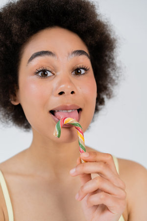 African american woman licking candy cane isolated on greyの写真素材
