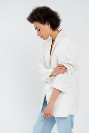 Side view of trendy african american woman rolling up sleeve of jacket isolated on greyの写真素材