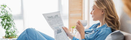 side view of carefree young woman reading travel life newspaper and holding cup of coffee in bedroom, bannerの写真素材