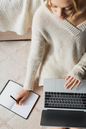 top view of freelancer taking notes on notebook while using laptopの写真素材